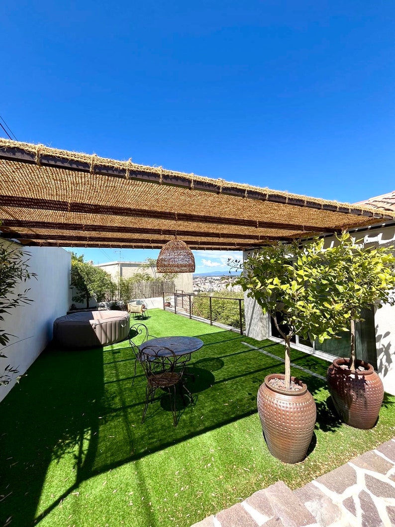 May include: A patio with a brown pergola, a small table and chairs, a hot tub, and two potted lemon trees. The patio is covered in artificial grass.
