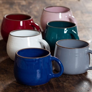 Può includere: Sei tazze in ceramica di diversi colori, tra cui rosso, bianco, rosa, verde acqua, grigio e blu. Le tazze hanno una forma arrotondata e un labbro leggermente svasato.