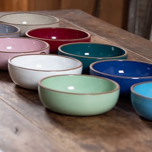 Peut inclure: Un ensemble de dix bols en céramique de différentes couleurs, dont le rose, le bleu, le vert, le blanc et le rouge. Les bols sont disposés en rangée sur une surface en bois.