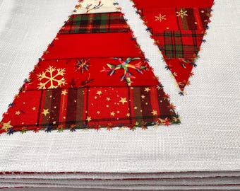 Könnte beinhalten: Weißes Weihnachts-Tischset aus Leinen mit applizierten roten und karierten Weihnachtsbäumen. Die Bäume bestehen aus verschiedenen roten Stoffen mit Schneeflocken- und Sternakzenten und sind mit farbigem Faden genäht.