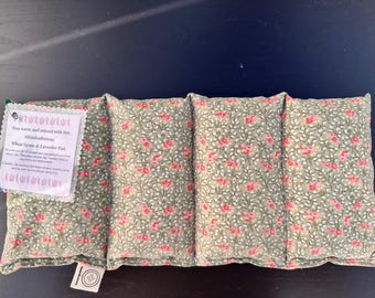 Könnte beinhalten: Ein rechteckiges Weizen- und Lavendel-Pad mit einem floralen Muster in Grün und Rosa. Das Pad hat ein Etikett mit der Aufschrift "Bleiben Sie warm und entspannt mit diesem Weizen- und Lavendel-Pad."