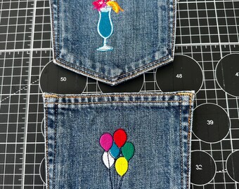 Könnte beinhalten: Zwei blaue Jeanstaschen mit gestickten Motiven. Die obere Tasche zeigt ein blaues Cocktailglas mit einem rosa Schirmchen und einer orangefarbenen Garnitur. Die untere Tasche zeigt ein Bündel aus fünf bunten Luftballons in Rot, Pink, Weiß, Gelb und Türkis.