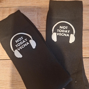 May include: A pair of black socks featuring the white text "NOT TODAY VECNA" and a white headphone graphic. The socks are presented on a wooden surface.