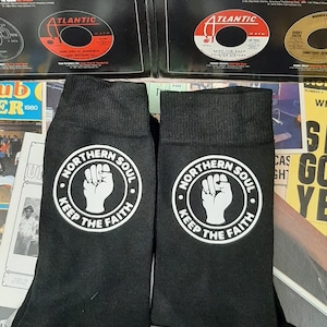 May include: A pair of black socks with a white circle design featuring a raised fist and the text "Northern Soul Keep The Faith".