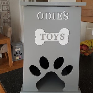 May include: Gray wooden dog toy storage box with a paw print cutout and the text "ODIE'S TOYS" on the front.
