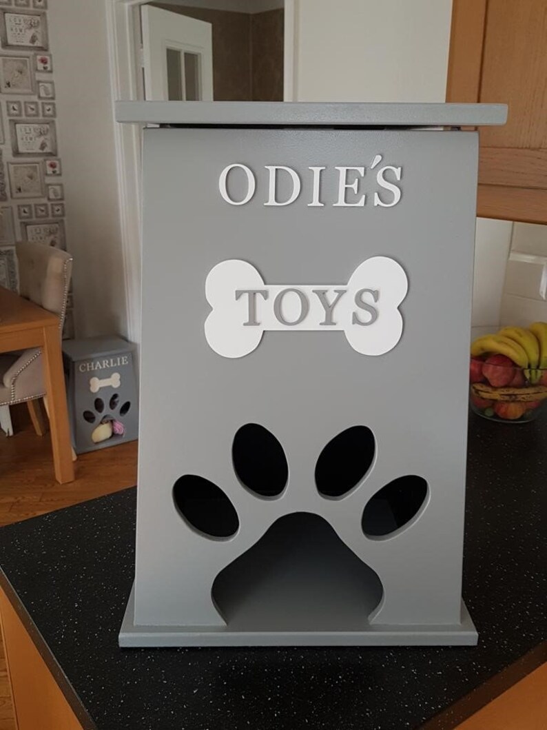 May include: Gray wooden dog toy storage box with a paw print cutout and the text "ODIE'S TOYS" on the front.