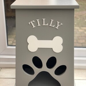 Peut inclure: Un conteneur de stockage de nourriture pour animaux de compagnie en bois gris, avec un motif d'os et d'empreinte de patte blancs. Le nom "TILLY" est affich&eacute; en lettres blanches. Forme rectangulaire, dessus plat.