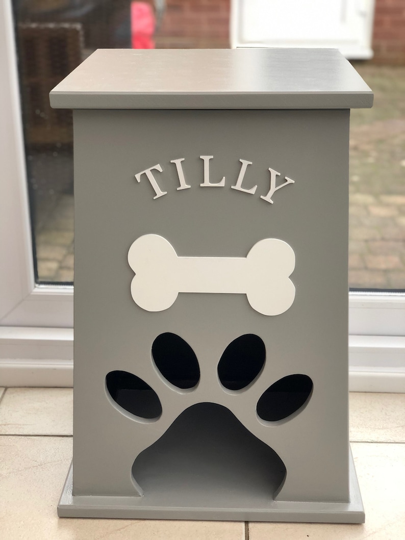 Peut inclure: Un conteneur de stockage de nourriture pour animaux de compagnie en bois gris, avec un motif d'os et d'empreinte de patte blancs. Le nom "TILLY" est affich&eacute; en lettres blanches. Forme rectangulaire, dessus plat.