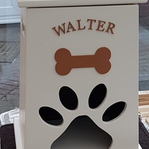 May include: White wooden dog food storage bin with a paw print cutout and a bone design. The bin has the name "WALTER" written on the front.