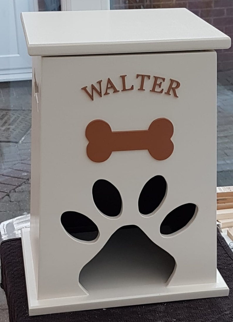 May include: White wooden dog food storage bin with a paw print cutout and a bone design. The bin has the name "WALTER" written on the front.