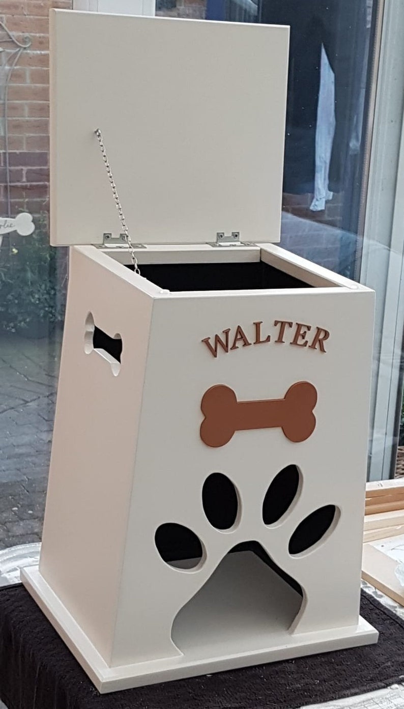 May include: White wooden dog food storage bin with a hinged lid and a paw print cutout. The bin has a brown bone and the name "WALTER" written on the front.