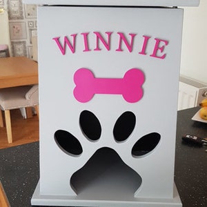May include: A gray wooden dog treat storage bin with a paw print cutout and a pink bone and the name "WINNIE" on the front.