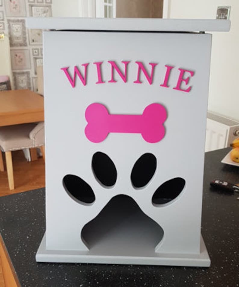May include: A gray wooden dog treat storage bin with a paw print cutout and a pink bone and the name "WINNIE" on the front.