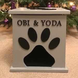 May include: A gray wooden pet food storage bin with a paw print cutout and the names "OBI & YODA" written on the front.