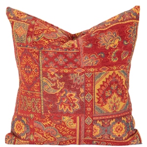 Könnte beinhalten: Ein dekoratives Zierkissen mit einem Patchwork-Design. Das Kissen hat einen roten Hintergrund mit detaillierten Mustern in Gelb, Blau und Orange. Die Muster umfassen Blumen- und Paisley-Motive und erzeugen ein reichhaltiges, strukturiertes Aussehen.
