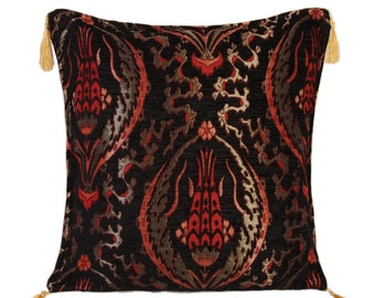 May include: A black cushion with a red and gold floral pattern. The cushion has tassels on each corner.