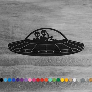 May include: Black silhouette of two aliens in a flying saucer, with one alien giving the peace sign. The saucer is against a woodgrain background.