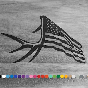 May include: Black graphic of an antler with the American flag incorporated into the design. The flag is waving, with stars and stripes visible. The image is set against a gray wood grain background.