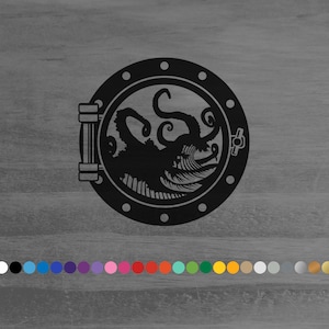 May include: Black metal wall art featuring a stylized kraken design within a circular porthole frame. The kraken has multiple tentacles and a detailed, open-mouthed head. The porthole has rivets and a hinged door. The background is a gray wooden surface.
