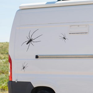 May include: A white van with three black spider decals on the side. The decals are of varying sizes and are placed in a random pattern.