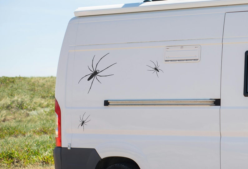 May include: A white van with three black spider decals on the side. The decals are of varying sizes and are placed in a random pattern.