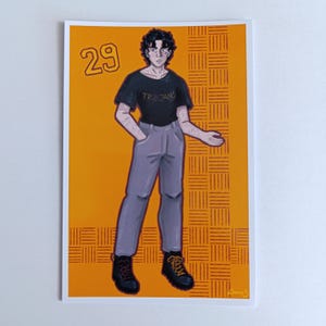 May include: Illustration of a person in a black t-shirt with "Trojans" and grey trousers. The artwork is set against an orange background with a grid pattern. The number "29" is in the upper left corner.