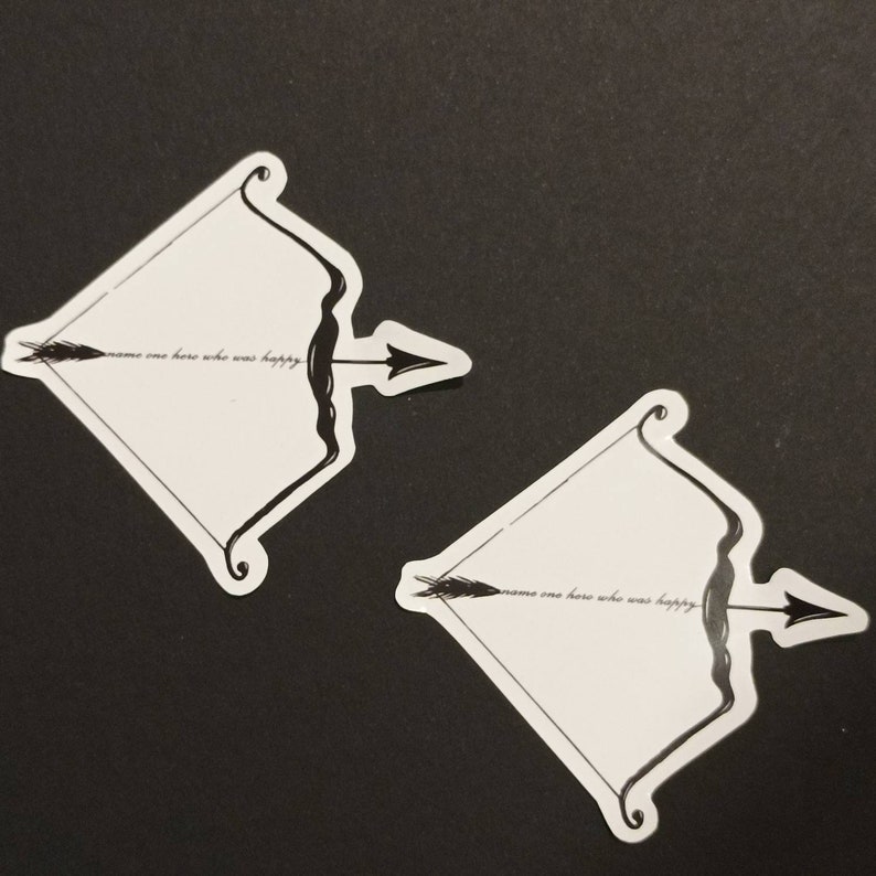 May include: Two white stickers with a black and white illustration of a bow and arrow. The text "name one hero who was happy" is written on each sticker.