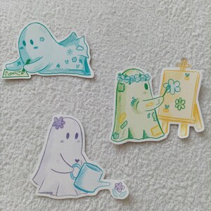 May include: Three cute ghost illustrations with different activities. One ghost is drawing on a canvas, another is holding a watering can, and the third is writing on a piece of paper.