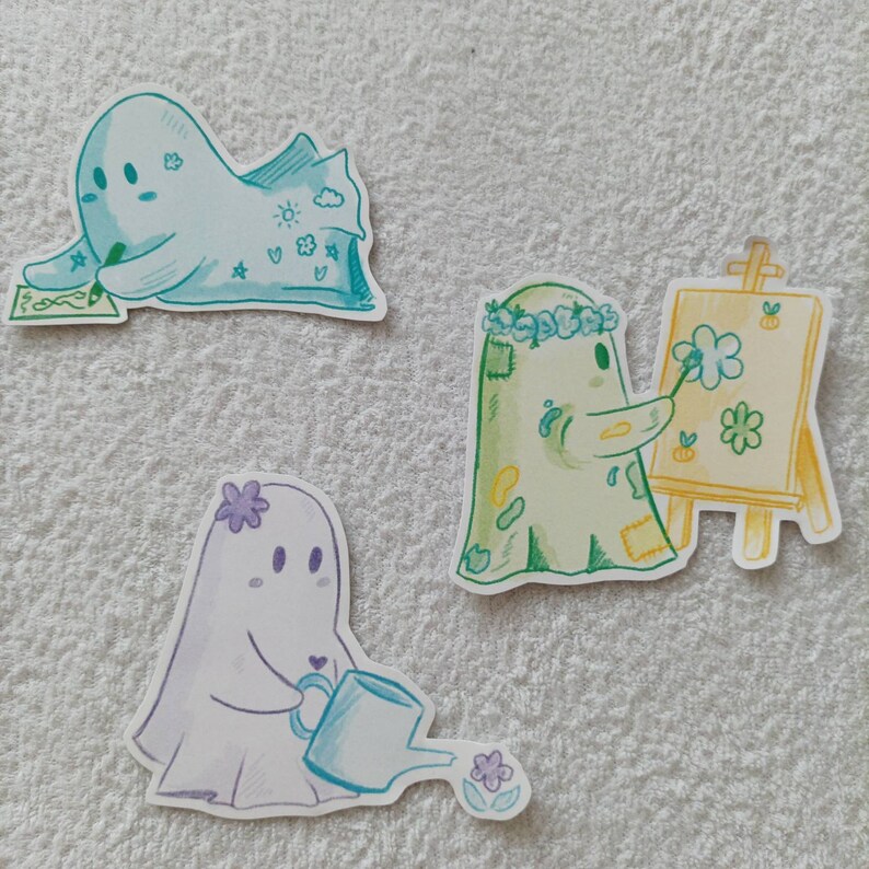 May include: Three cute ghost illustrations with different activities. One ghost is drawing on a canvas, another is holding a watering can, and the third is writing on a piece of paper.