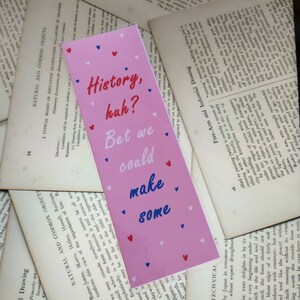 May include: Pink bookmark with the text "History, huh? Bet we could make some" in blue and white lettering. The bookmark is decorated with small red and white hearts.