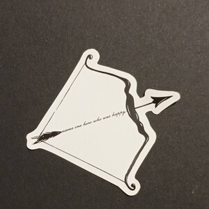 May include: A white sticker with a black and white illustration of a bow and arrow. The sticker has the text "name one hero who was happy" written on it.