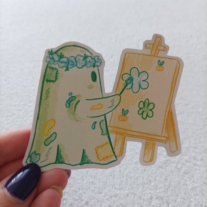 May include: A green ghost with a blue flower crown is painting a flower on a yellow easel. The ghost has green and yellow paint splatters on it.