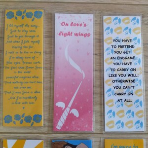 May include: Three bookmarks with different designs and quotes. The first bookmark is yellow with a quote about love and a white heart. The second bookmark is pink with a white wand with wings and the quote "On love's light wings". The third bookmark is blue and yellow with a quote about pretending to get an endgame and the words "You have to carry on like you will; otherwise you can't carry on at all."