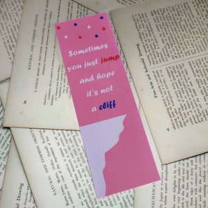 May include: Pink bookmark with a white silhouette of a cliff and the text "Sometimes you just jump and hope it's not a cliff" in white with blue and red stars.