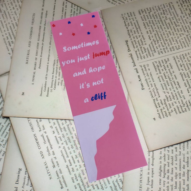 May include: Pink bookmark with a white silhouette of a cliff and the text "Sometimes you just jump and hope it's not a cliff" in white with blue and red stars.