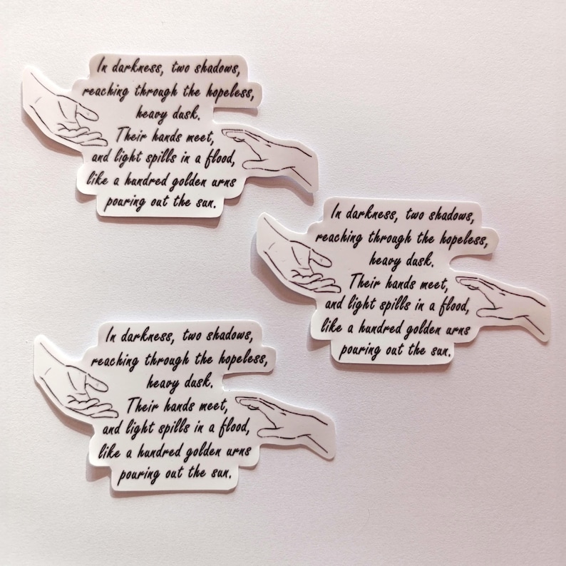 Peut inclure: Trois autocollants blancs avec du texte noir et un dessin simple de deux mains se tendant l'une vers l'autre. Le texte dit : "Dans les t&eacute;n&egrave;bres, deux ombres, atteignant &agrave; travers le d&eacute;sespoir, la lourde t&acirc;che. Leurs mains se rencontrent, et la lumi&egrave;re se r&eacute;pand en un flot, comme une centaine de bras dor&eacute;s versant le soleil."