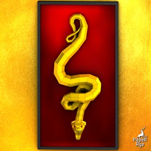 May include: A gold papercraft snake sculpture in a red frame. The snake is curled up in a coil with its head facing forward. The sculpture is made of paper and is very detailed.