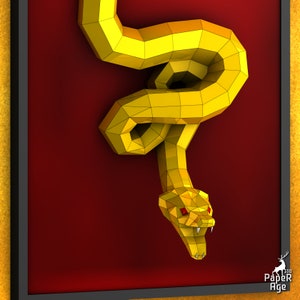 May include: A golden papercraft snake with red eyes, hanging on a red background. The snake is curled up in a coil with its head facing forward. The snake is made of paper and has a 3D effect.