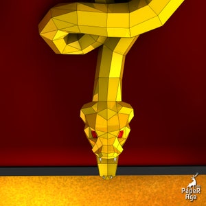 May include: A yellow papercraft snake with red eyes hangs upside down, its head facing the viewer. The snake is made of folded paper and has a textured, polygonal appearance. The background is a solid red color.