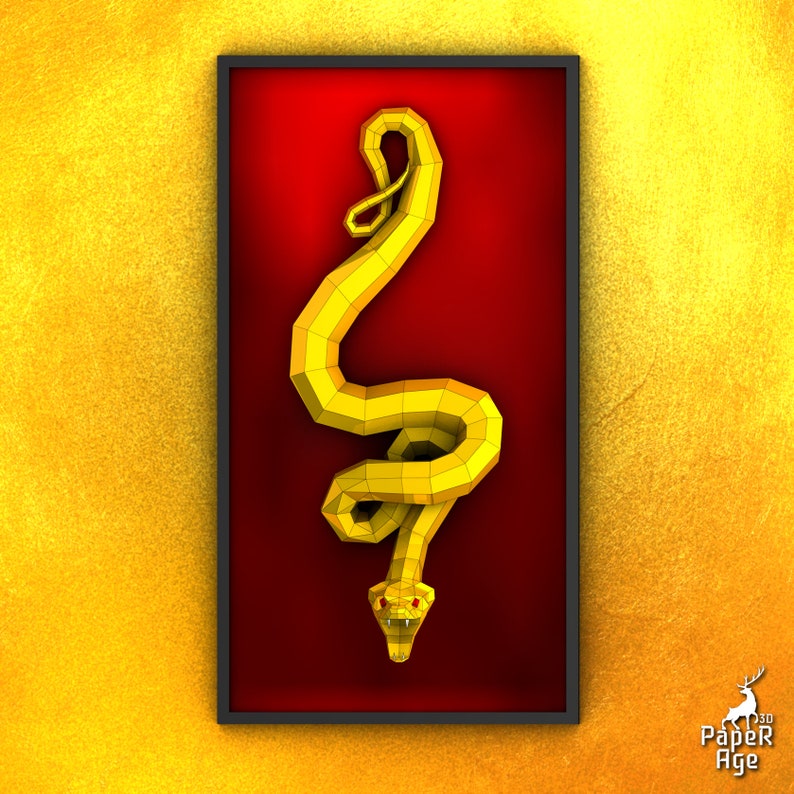 May include: A yellow paper snake sculpture in a red frame. The snake is curled up with its head facing down. The frame is black and has a white border.