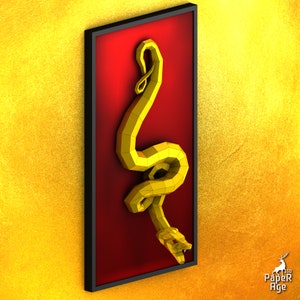 May include: A gold papercraft snake sculpture in a black frame against a red background. The snake is curled up in a coil with its head facing down.