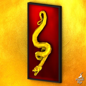 May include: A golden papercraft snake sculpture in a red frame. The snake is curled up with its head facing forward and its mouth open. The sculpture is a 3D paper model.