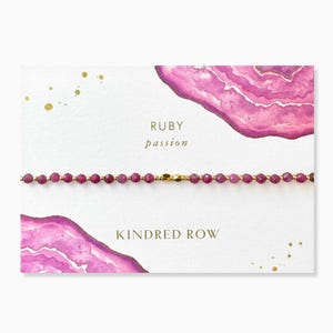 May include: A delicate bracelet made with ruby beads and a gold clasp. The card reads "RUBY passion" and "KINDRED ROW".