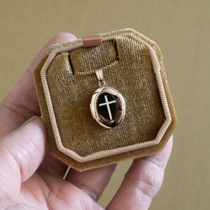 May include: A gold oval locket with a black enamel cross pendant. The locket is in a velvet box.