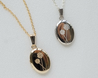 May include: Two oval-shaped locket necklaces. One is gold-toned, the other silver-toned. Each locket features a delicate floral design and hangs from a matching chain. The background is a soft, off-white fabric.