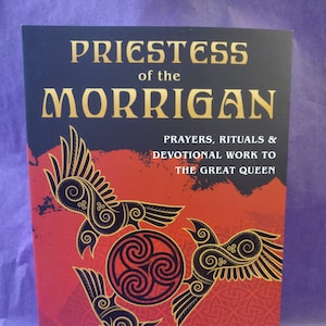 May include: Book cover with a black background and gold lettering that reads "Priestess of the Morrigan". The cover features a red background with three black stylized birds with gold accents surrounding a gold Celtic knot. The text "Prayers, Rituals & Devotional Work to the Great Queen" is in gold lettering. The author's name, "Stephanie Woodfield", is in gold lettering at the bottom of the cover.