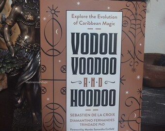 May include: A brown book with the title "VODOU VOODOO AND HOODOO" in white text. The book explores the evolution of Caribbean magic and features a foreword by Mambo Samantha Corfield.