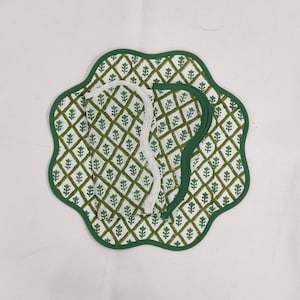 May include: Three green and white patterned placemats with scalloped edges. The placemats are made of fabric and have a diamond pattern with green leaves.