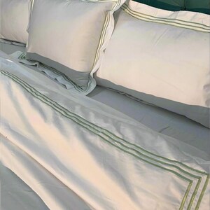 May include: White bed linen with green trim. The linen is folded and arranged on a bed with a green headboard.