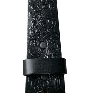 K&ouml;nnte beinhalten: Schwarzer Lederg&uuml;rtel mit einem gepr&auml;gten Blumenmuster. Der G&uuml;rtel hat eine Schnalle und einen Riemenhalter.